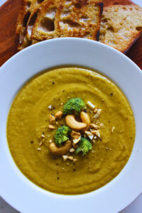 overhead image of sweet potato broccoli soup topped with black pepper, cashews and broccoli. served with a side of sourdough bread