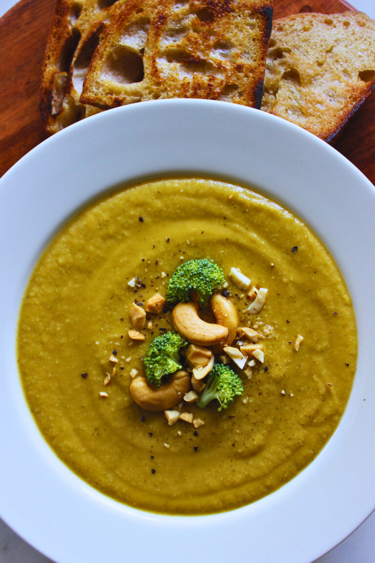 overhead image of sweet potato broccoli soup topped with black pepper, cashews and broccoli. served with a side of sourdough bread