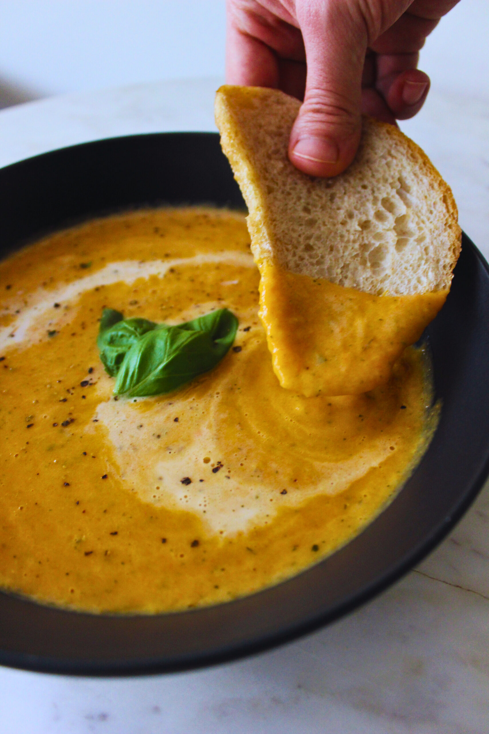 image of hand dipping fresh sourdough bread into creamy roasted veggie soup